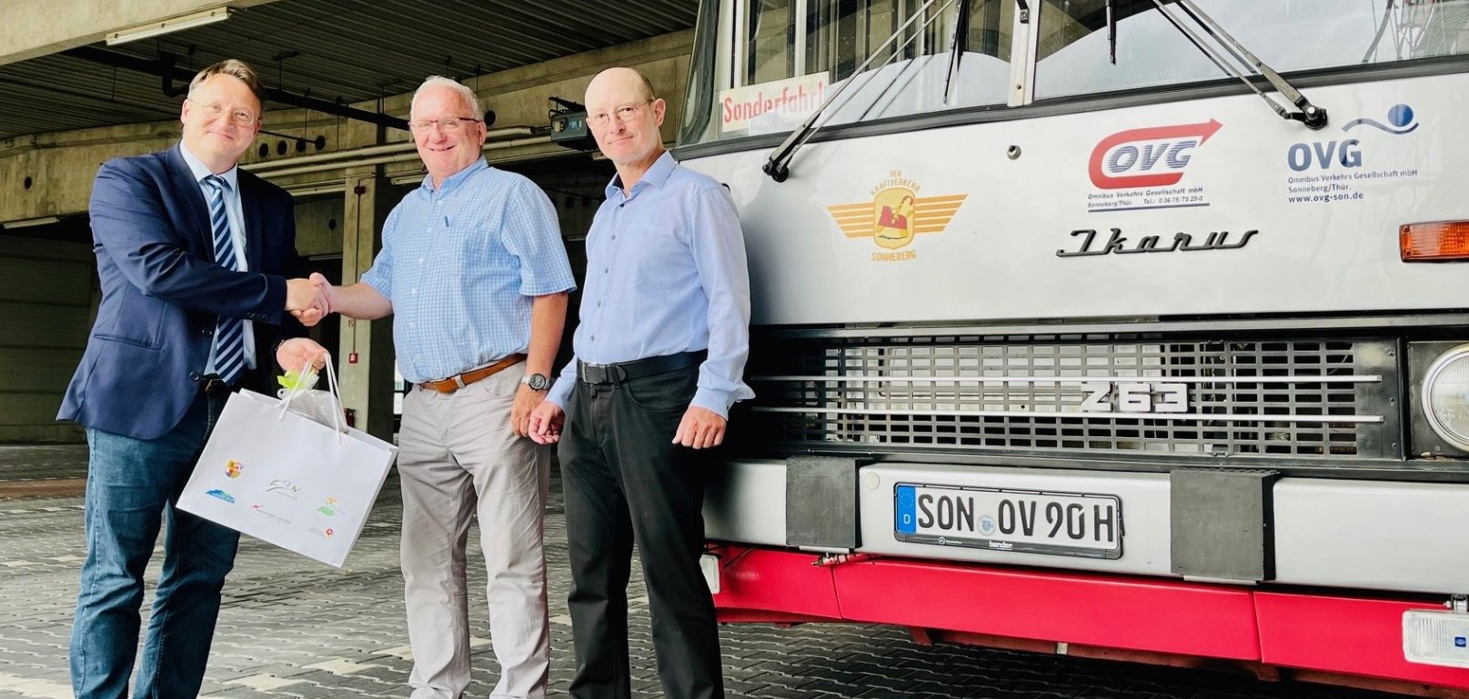 Jubilar Klaus Dieter Schneider (M.) mit den Gratulanten Landrat Robert Sesselmann (l.) und dem Hauptamtlichen Beigeordneten Andreas Groß (r.) neben dem IKARUS-Nostalgiefahrzeug der OVG 