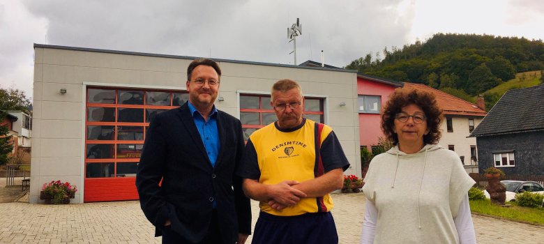 Bürgermeisterin Ute Müller-Gothe (r.), Kamerad Marko Weiß vom Löschzug West der Gemeinde Frankenblick (M.) und Landrat Robert Sesselmann vor dem Feuerwehrgerätehaus Rauenstein. Auf dem Dach im Hintergrund ist die neue Sirene erkennbar.